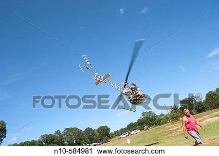 Stock Image - Man walking past a helicopter in flight.. Fotosearch