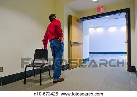 Man, wearing a red shirt, standing next to an empty chair that is near open doors in a college building View Large Photo Image Stock Photography - Man, wearing a red shirt, standing next to an empty chair that is near open doors in a college building. Fotosearch