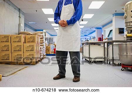 Stock Photo - Man, wearing an apron, standing in the middle of a dessert factory.. Fotosearch