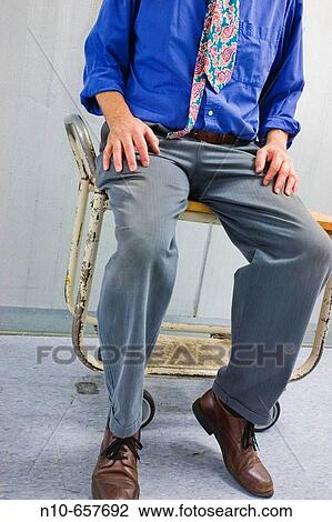 Stock Image - Man, wearing an uneven tie, sitting on a rolling cart.. Fotosearch