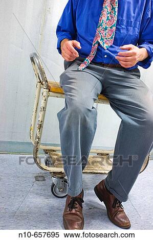 Man, wearing an uneven tie, sitting on a rolling cart. View Large Photo Image Stock Photography - Man, wearing an uneven tie, sitting on a rolling cart.. Fotosearch