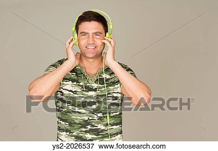 Stock Photo - Man wearing camouflage t-shirt listen to music with green headphones.. Fotosearch