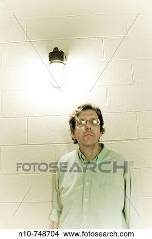 Man wearing glasses, standing underneath a bright light. View Large Photo Image Picture - Man wearing glasses, standing underneath a bright light.. Fotosearch