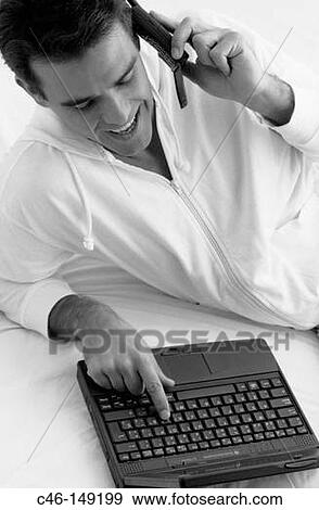 Stock Photo - Man with a laptop computer talking on cellular phone. Fotosearch