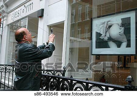 Stock Photograph - Man with cigar snapping photo with cell phone camera. Taken in the Mayfair section of London, England. UK. Fotosearch