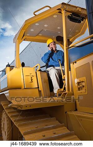 Man with hard hat on bulldozer using mobile phone. View Large Photo Image Stock Photo - Man with hard hat on bulldozer using mobile phone.. Fotosearch