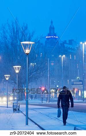 Man with head bent walking in snow storm through city at night, Stockholm, Sweden. View Large Photo Image Picture - Man with head bent walking in snow storm through city at night, Stockholm, Sweden.. Fotosearch
