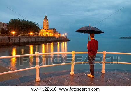 Stock Photograph - Man with umbrella on the promenade, night view. Gij? n, Asturias province, Spain.. Fotosearch