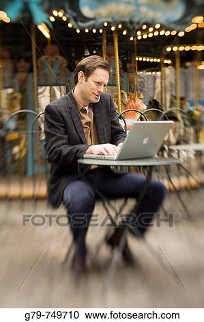 Man working outside in a park, typing on laptop and talking on cell phone in front of carousel. View Large Photo Image Stock Image - Man working outside in a park, typing on laptop and talking on cell phone in front of carousel.. Fotosearch