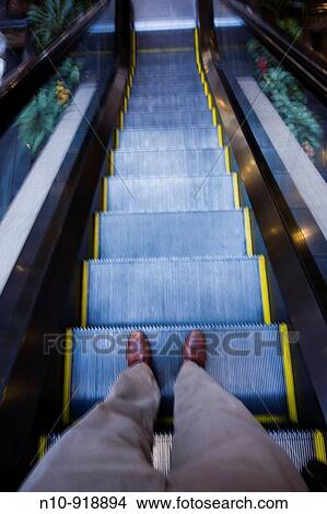 Picture - Man's feet as he goes on a down escalator. Fotosearch
