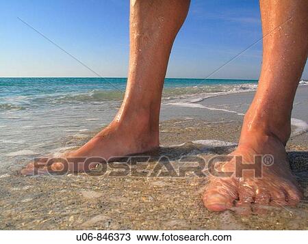 Stock Image - Man's feet in the water at beach. Fotosearch