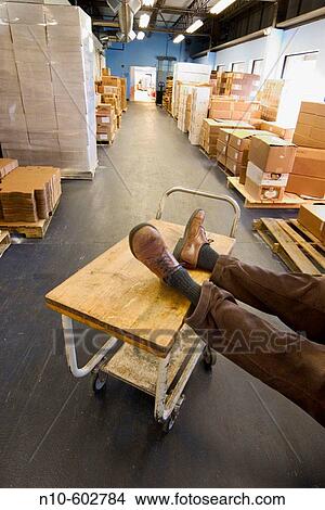 Man's feet, wearing shoes, resting on a rolling cart in a factory's storage area. View Large Photo Image Picture - Man's feet, wearing shoes, resting on a rolling cart in a factory's storage area.. Fotosearch