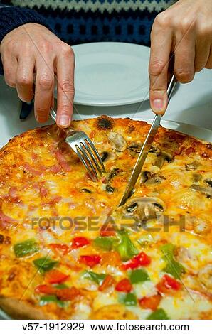 Stock Photo - Man's hand cutting a piece of pizza. Close view.. Fotosearch