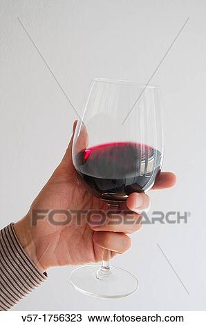 Stock Image - Man's hand holding a glass of red wine, tasting it. Fotosearch
