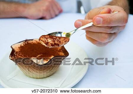 Stock Image - Man's hand offering a spoonful of tiramisu. Close view.. Fotosearch