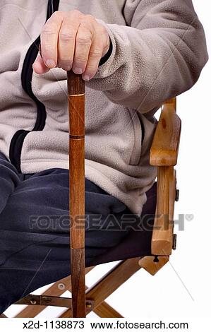 Stock Image - Mature man seated holding a walking stick. Fotosearch
