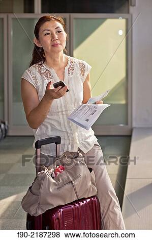 Stock Photo - Mature woman checks air ticket at airport, Tokyo, Japan.. Fotosearch