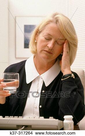 Picture - Mature woman with glass of water, suffering from headache. Fotosearch