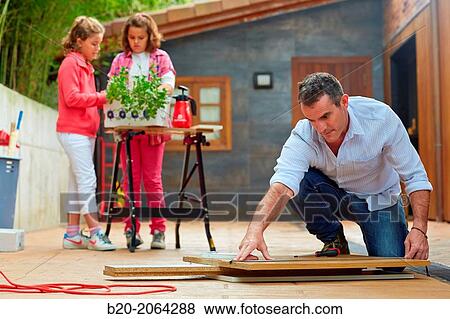 Stock Photo - Measuring a wooden board. Tinkering. Father and children doing DIY.. Fotosearch