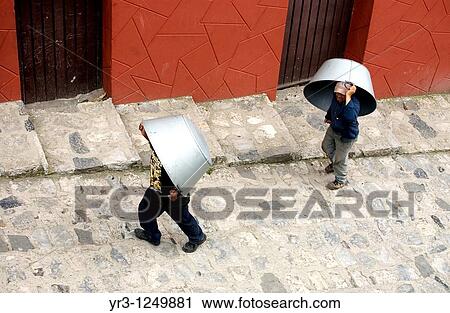 Stock Image - Men carry large metal pans for sale or barter in the Sunday market in Cuetzalan del Progreso, Mexico.. Fotosearch