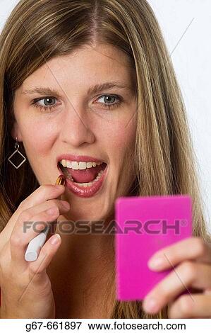 Mid 20's caucasian woman looking into hand held mirror with applying make up to her lips View Large Photo Image Stock Photo - Mid 20's caucasian woman looking into hand held mirror with applying make up to her lips. Fotosearch