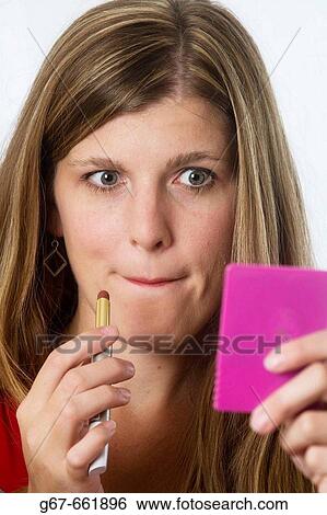 Mid 20's caucasian woman looking into hand held mirror with applying make up to her lips View Large Photo Image Stock Photograph - Mid 20's caucasian woman looking into hand held mirror with applying make up to her lips. Fotosearch
