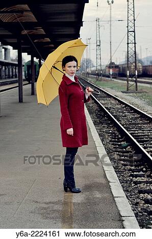 Mid adult woman standing on railroad station platform holding umbrella. View Large Photo Image Stock Image - Mid adult woman standing on railroad station platform holding umbrella.. Fotosearch
