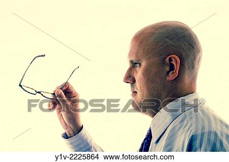 Picture - Middle-age bald man holding his glasses.. Fotosearch