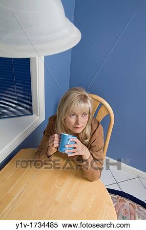 Stock Photography - Middle-age blond woman drinking coffee in her kitchen. Fotosearch