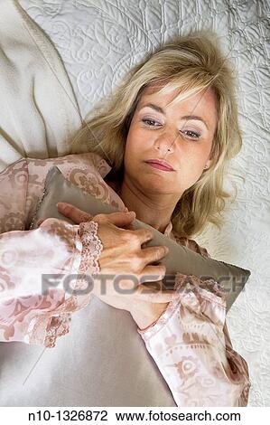 Stock Image - Middle-age blond woman lying in bed. Fotosearch