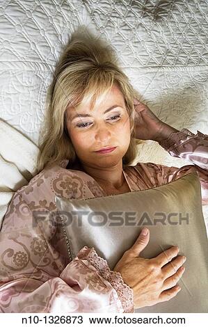 Stock Image - Middle-age blond woman lying in bed. Fotosearch