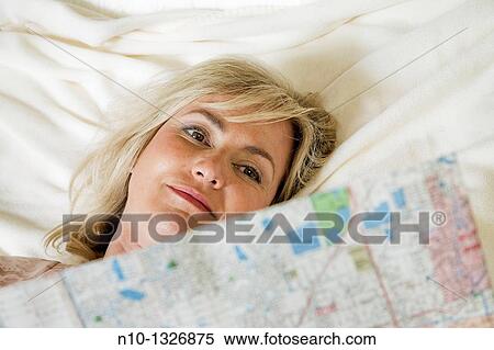 Stock Photography - Middle-age blond woman reading a map in bed. Fotosearch