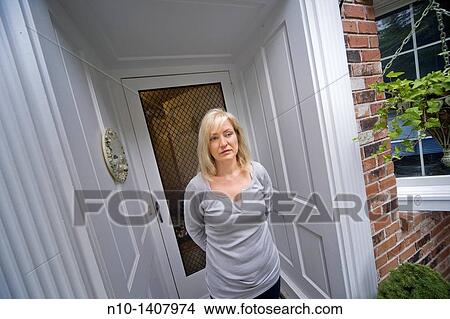Picture - Middle-age blond woman standing by her front door. Fotosearch