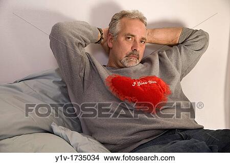 Picture - Middle-age man holding a heart-shaped pillow with? I Love You? written on it. Fotosearch