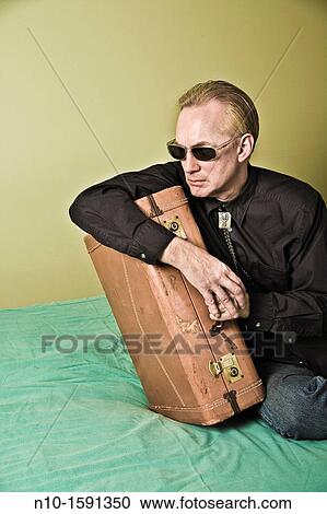 Middle-age man sitting on a bed with a suitcase View Large Photo Image Stock Image - Middle-age man sitting on a bed with a suitcase. Fotosearch