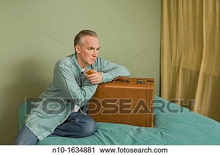 Middle-age man sitting on a bed with a suitcase View Large Photo Image Stock Image - Middle-age man sitting on a bed with a suitcase. Fotosearch