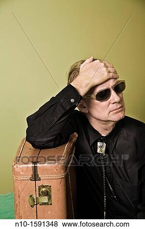 Stock Photo - Middle-age man sitting on a bed with a suitcase. Fotosearch