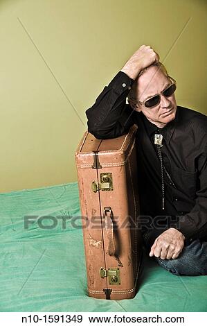Stock Photo - Middle-age man sitting on a bed with a suitcase. Fotosearch
