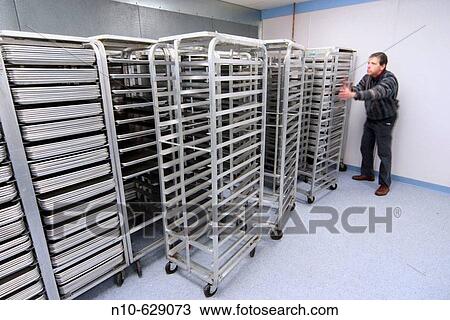 Stock Image - Middle age man standing near metal tray racks in a factory.. Fotosearch