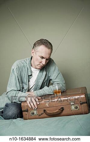 Middle-age man with a drink setting on a suitcase View Large Photo Image Picture - Middle-age man with a drink setting on a suitcase. Fotosearch