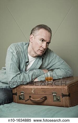 Stock Photography - Middle-age man with a drink setting on a suitcase. Fotosearch