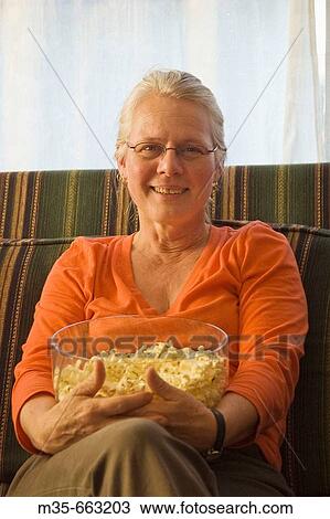 Middle age woman sitting on couch holding popcorn View Large Photo Image Stock Image - Middle age woman sitting on couch holding popcorn. Fotosearch