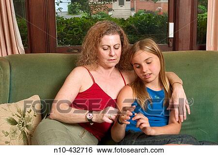 Stock Photograph - Middle age woman with her arm around a preteen girl, sitting together on a sofa. Fotosearch