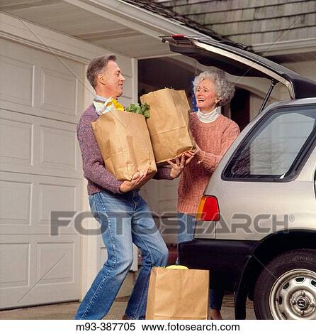 Stock Photography - Middle-aged couple hapily unloading groceries from car near garage entrance. Fotosearch