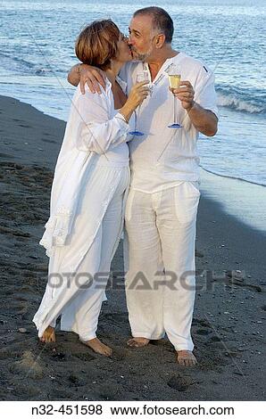 Middle-aged couple on the beach, holding champagne glasses View Large Photo Image Stock Photo - Middle-aged couple on the beach, holding champagne glasses. Fotosearch