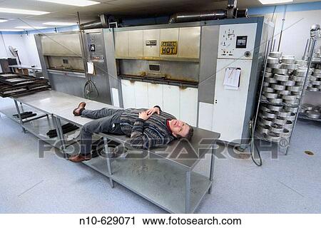 Middle aged man lying on a metal table in a factory. View Large Photo Image Stock Image - Middle aged man lying on a metal table in a factory.. Fotosearch