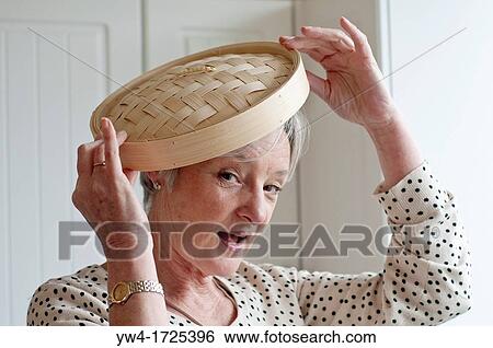 Stock Photograph - Middle aged woman playing with bamboo lid in kitchen. Fotosearch