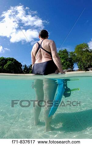 Stock Photo - Middle aged women in one piece swim suit snorkelling over sandy on tropical beach. Ha`apai Group, Tonga. South Pacific Ocean.. Fotosearch