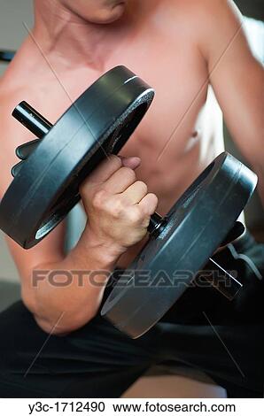 Midsection of young man curling dumbbell at a gym View Large Photo Image Stock Image - Midsection of young man curling dumbbell at a gym. Fotosearch