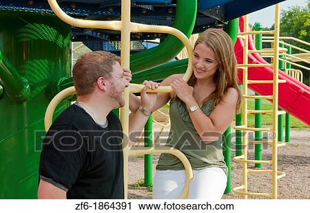 Stock Image - Midwest couple aged 22 playing and dating in park at monkey bars and hugging playing. Fotosearch